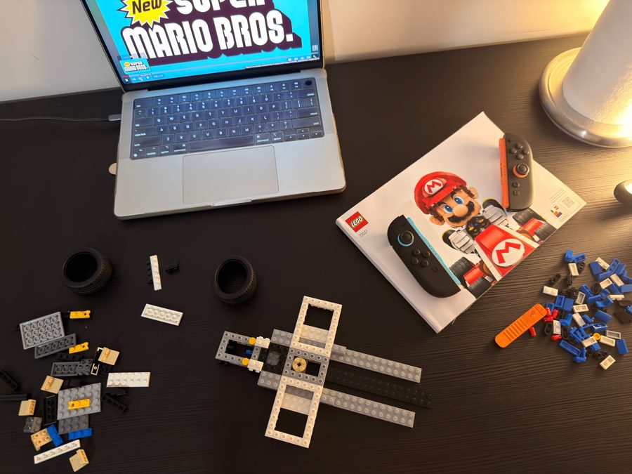 A LEGO Mario Kart set mid-build next to a laptop playing Super Mario Bros.